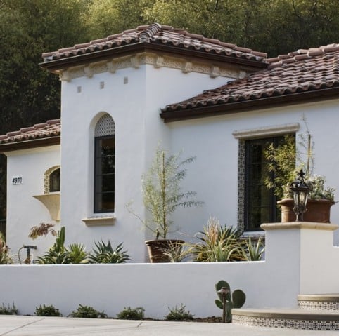 White stucco house with clay tile roof, arched windows, and desert landscaping in front.